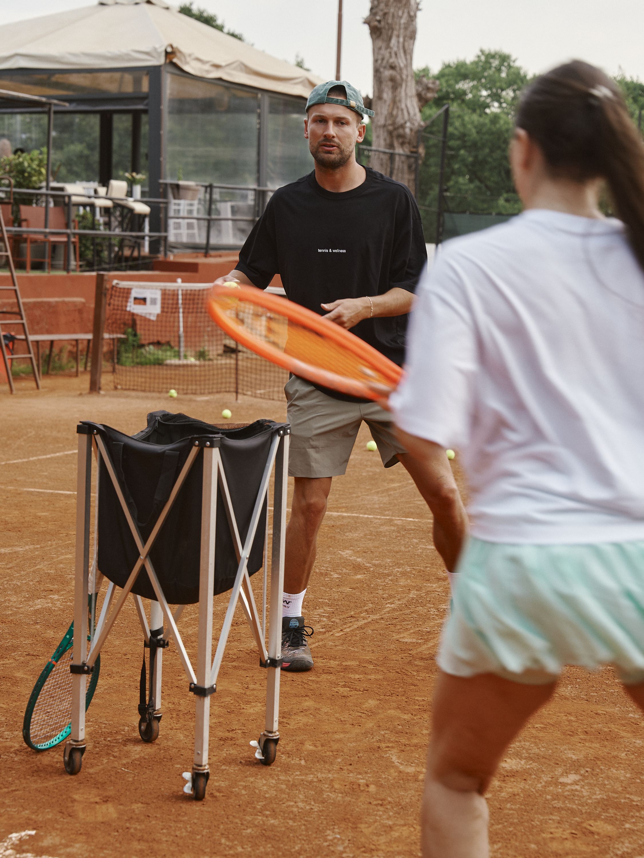 Coach feeding balls during a session on the clay